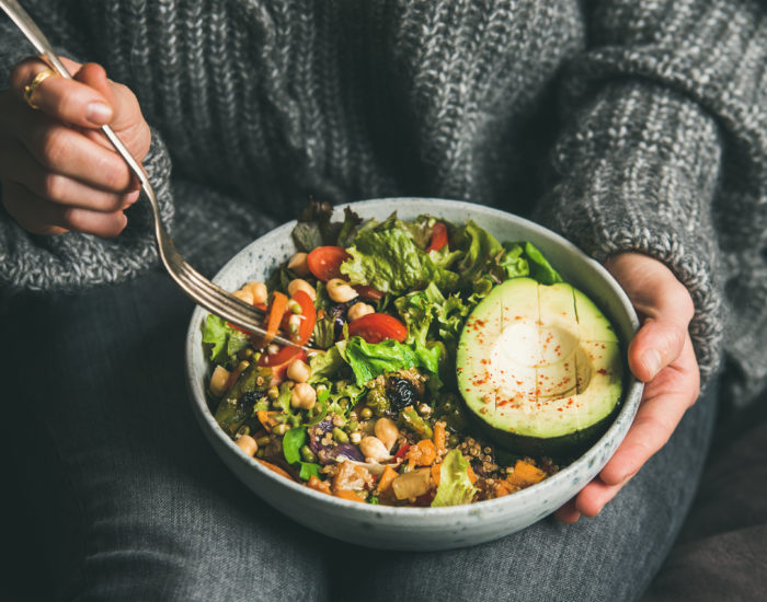 Woman eating healthy vegetarian dinner from Buddha bowl, close-up Healthy vegetarian dinner. Woman in jeans and warm sweater holding bowl with fresh salad, avocado, grains, beans, roasted vegetables, close-up. Superfood, clean eating, vegan, dieting food concept
